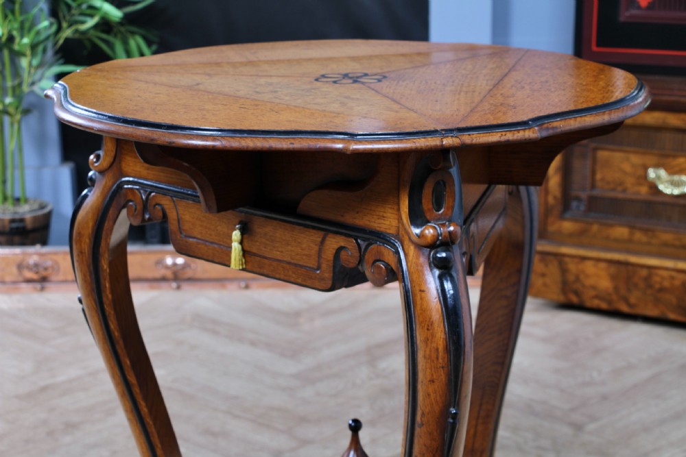 A Victorian Aesthetic Movement oak handkerchief table featuring ebonised accents, curved legs, and a triangular drop-leaf top with a central inlaid floral motif. View VIII