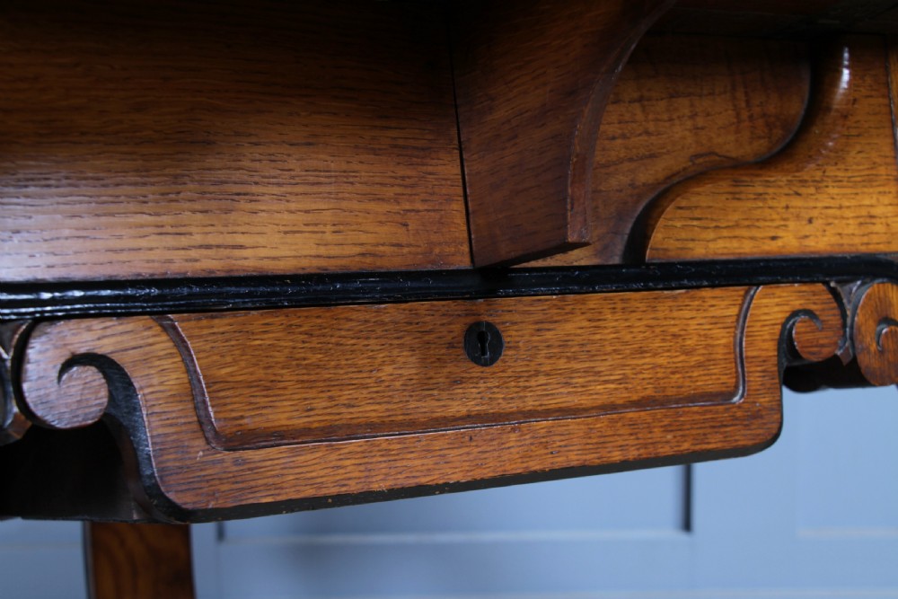 A Victorian Aesthetic Movement oak handkerchief table featuring ebonised accents, curved legs, and a triangular drop-leaf top with a central inlaid floral motif. View IX