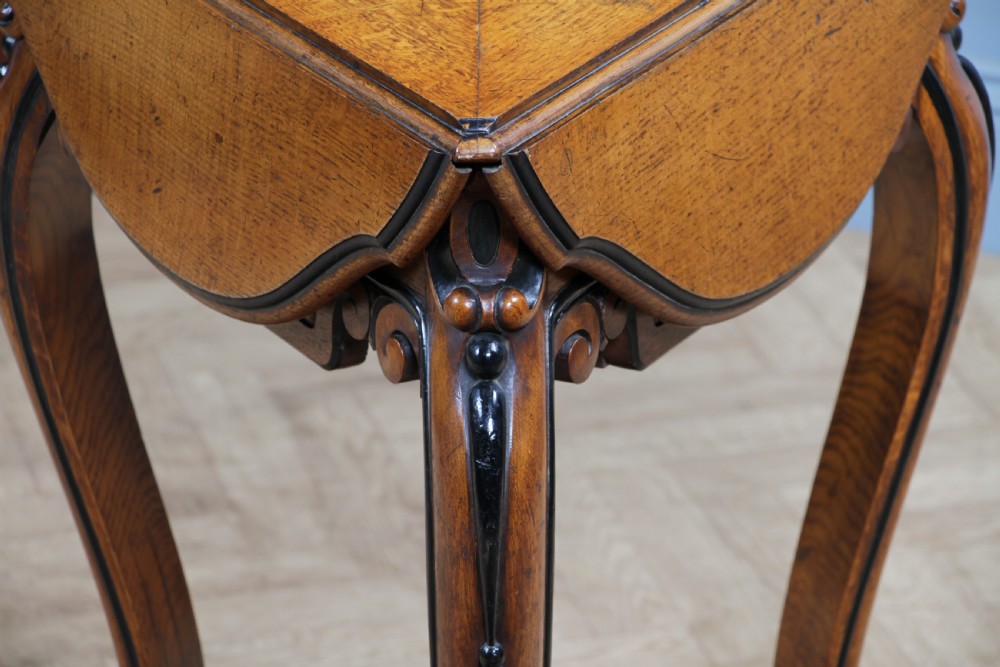 A Victorian Aesthetic Movement oak handkerchief table featuring ebonised accents, curved legs, and a triangular drop-leaf top with a central inlaid floral motif. View XII