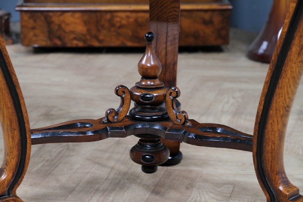 A Victorian Aesthetic Movement oak handkerchief table featuring ebonised accents, curved legs, and a triangular drop-leaf top with a central inlaid floral motif. View XIV