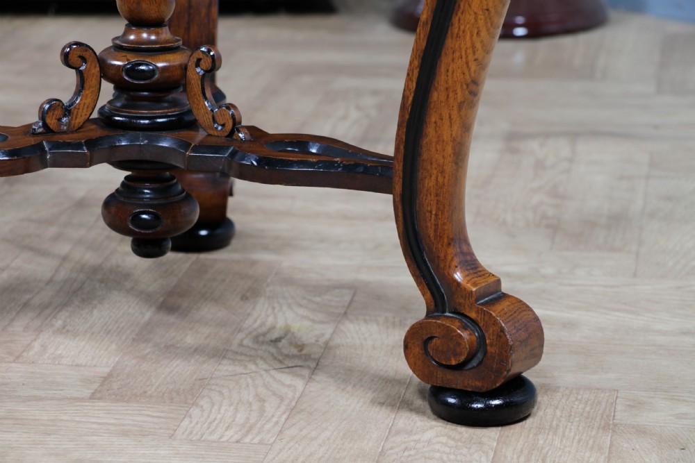 A Victorian Aesthetic Movement oak handkerchief table featuring ebonised accents, curved legs, and a triangular drop-leaf top with a central inlaid floral motif. View XV