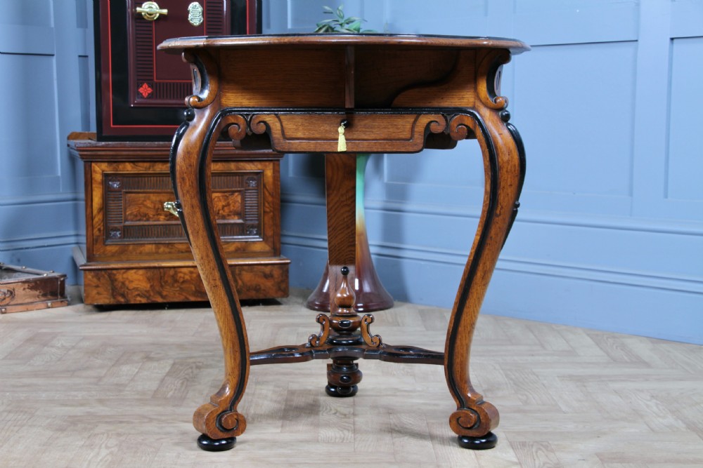 A Victorian Aesthetic Movement oak handkerchief table featuring ebonised accents, curved legs, and a triangular drop-leaf top with a central inlaid floral motif. View XVI