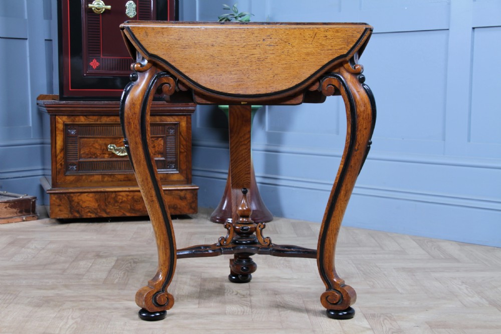 A Victorian Aesthetic Movement oak handkerchief table featuring ebonised accents, curved legs, and a triangular drop-leaf top with a central inlaid floral motif. View XVII