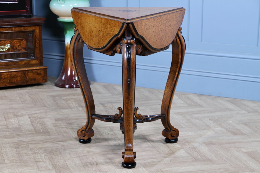 A Victorian Aesthetic Movement oak handkerchief table featuring ebonised accents, curved legs, and a triangular drop-leaf top with a central inlaid floral motif. View XVIII