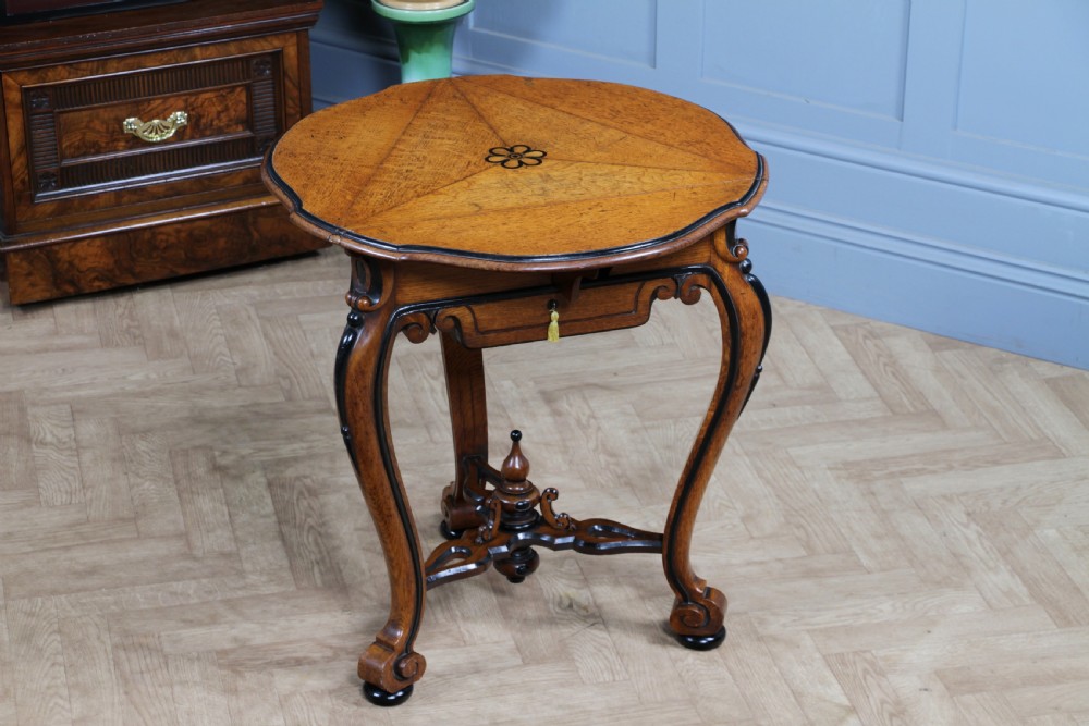 A Victorian Aesthetic Movement oak handkerchief table featuring ebonised accents, curved legs, and a triangular drop-leaf top with a central inlaid floral motif. View XX
