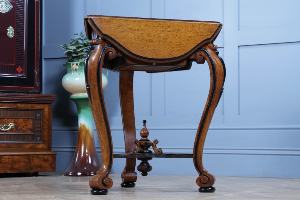 A Victorian Aesthetic Movement oak handkerchief table featuring ebonised accents, curved legs, and a triangular drop-leaf top with a central inlaid floral motif. View XXI