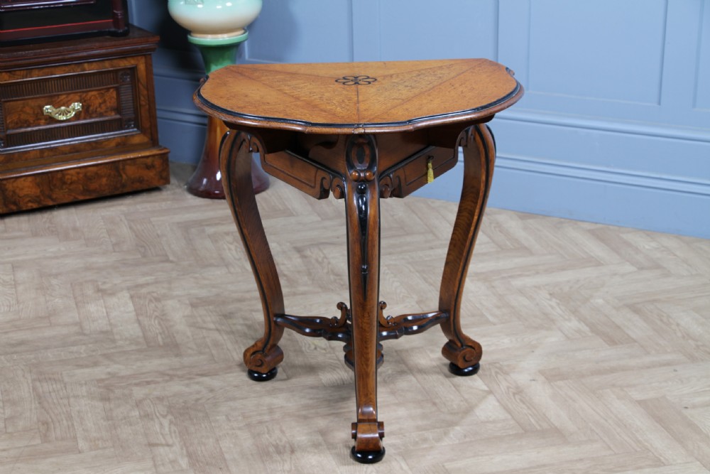 A Victorian Aesthetic Movement oak handkerchief table featuring ebonised accents, curved legs, and a triangular drop-leaf top with a central inlaid floral motif. View XXII