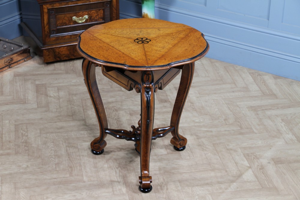 A Victorian Aesthetic Movement oak handkerchief table featuring ebonised accents, curved legs, and a triangular drop-leaf top with a central inlaid floral motif. View XXIII