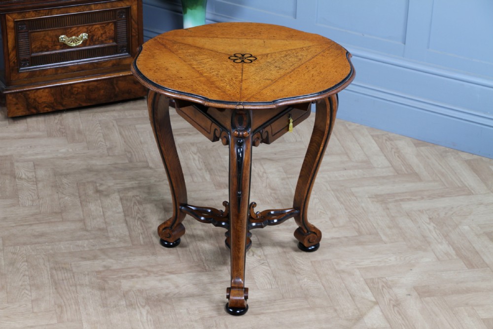 A Victorian Aesthetic Movement oak handkerchief table featuring ebonised accents, curved legs, and a triangular drop-leaf top with a central inlaid floral motif. View XXIV