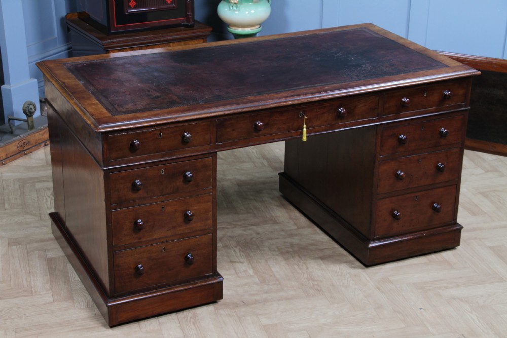A Victorian mahogany pedestal desk featuring twin drawer pedestals, a dark leather writing inset, and a matching angled writing slope. View VI