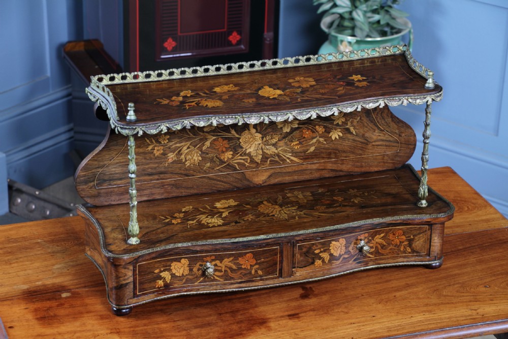 A French Napoleon III rosewood tabletop etagere featuring two tiered shelves decorated with floral marquetry, gilt metal mounts, a gallery rail, and two small base drawers.