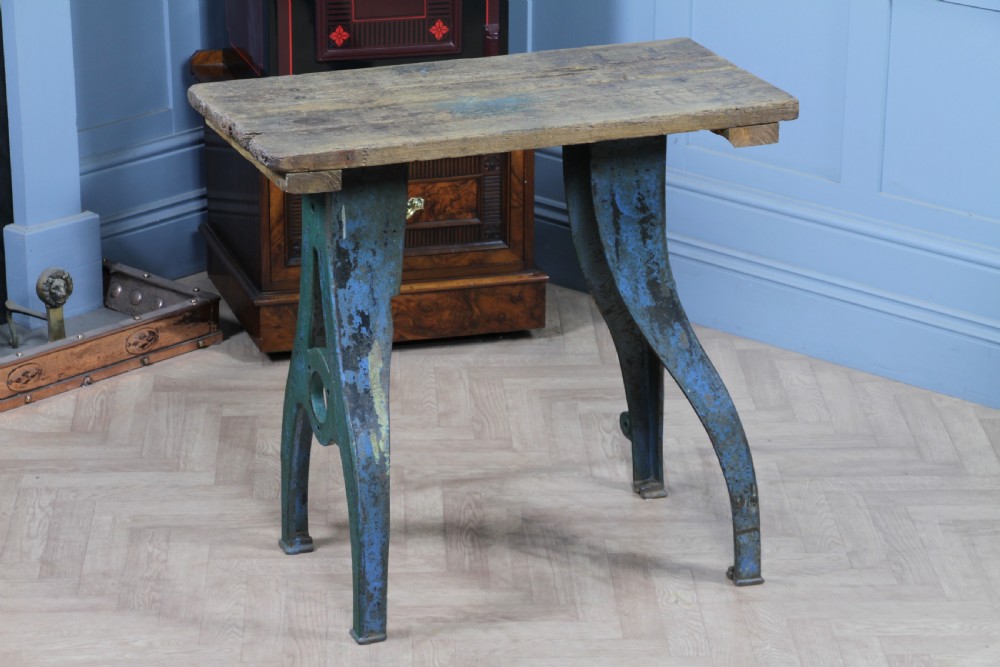 An industrial console table featuring distressed blue painted cast iron machinery legs supporting a rectangular reclaimed pine top.