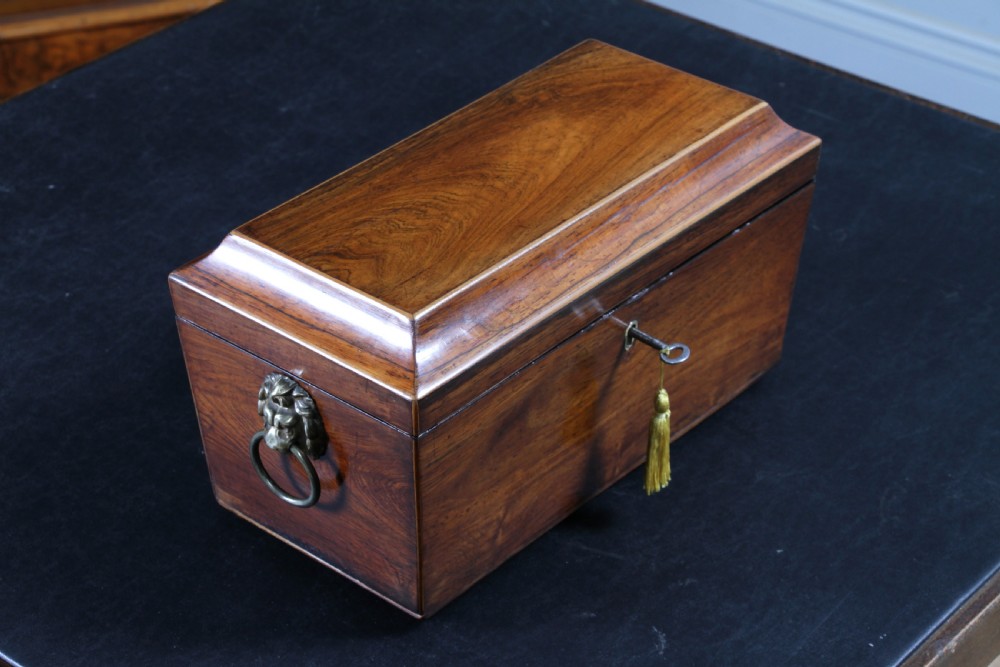 A Georgian rosewood sarcophagus-form tea caddy featuring stringing inlay, brass lion-mask side handles, and a keyhole with a tasselled key. View VI