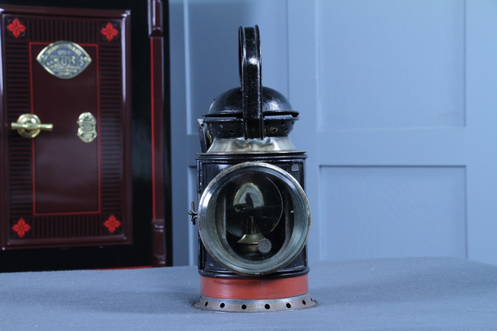 An antique black painted iron GWR railway hand lantern featuring a circular glass lens, top handle, brass accents, and a red painted band near the base. View II