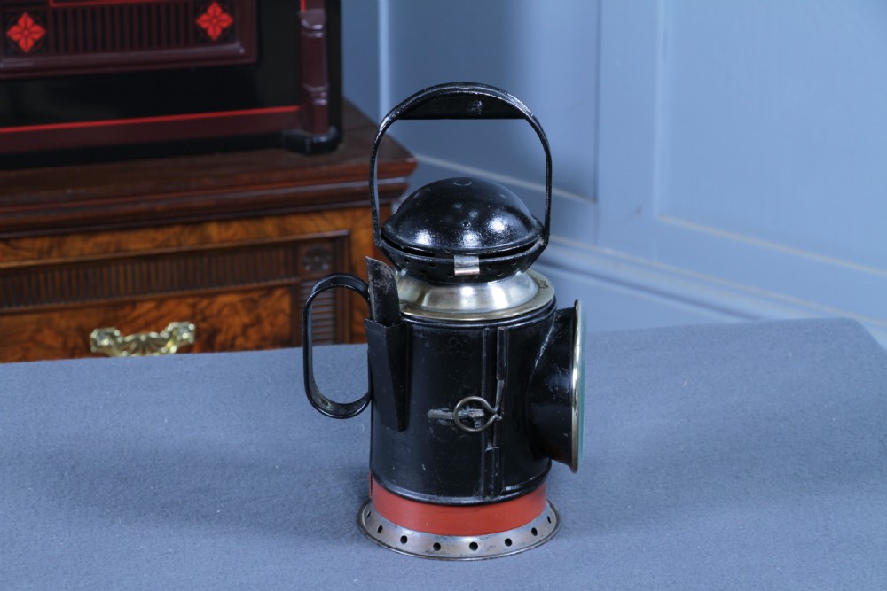 An antique black painted iron GWR railway hand lantern featuring a circular glass lens, top handle, brass accents, and a red painted band near the base. View III