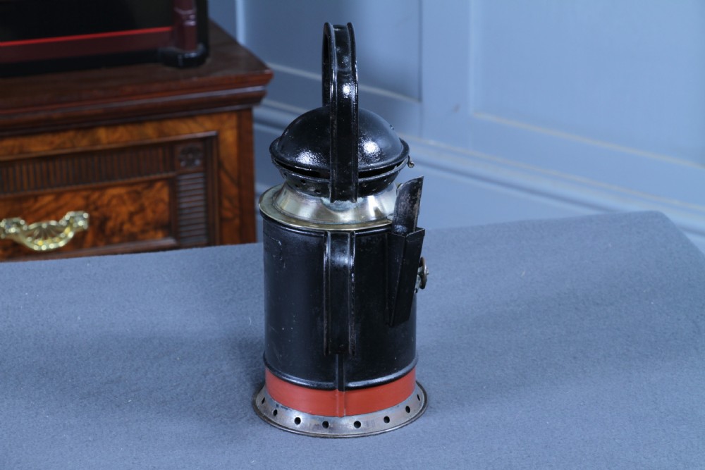 An antique black painted iron GWR railway hand lantern featuring a circular glass lens, top handle, brass accents, and a red painted band near the base. View IV