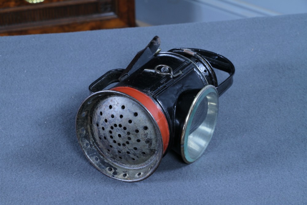 An antique black painted iron GWR railway hand lantern featuring a circular glass lens, top handle, brass accents, and a red painted band near the base. View VI