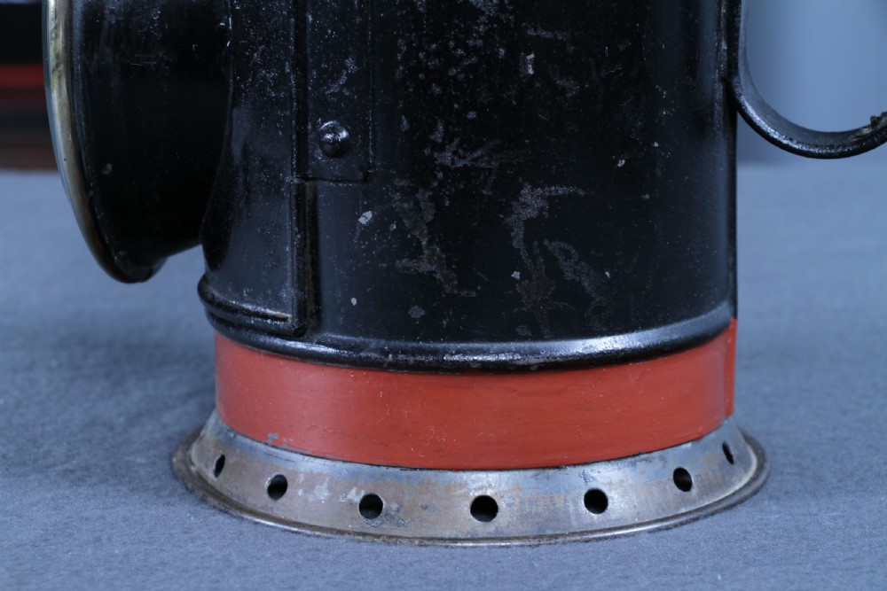 An antique black painted iron GWR railway hand lantern featuring a circular glass lens, top handle, brass accents, and a red painted band near the base. View VII