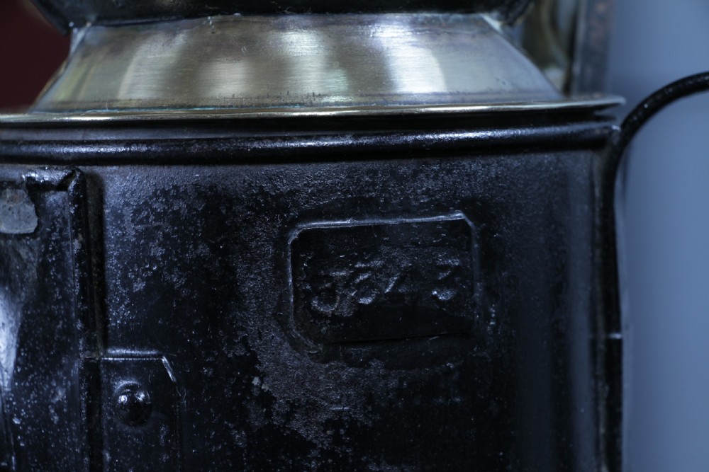 An antique black painted iron GWR railway hand lantern featuring a circular glass lens, top handle, brass accents, and a red painted band near the base. View IX