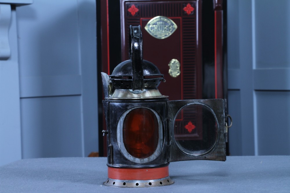 An antique black painted iron GWR railway hand lantern featuring a circular glass lens, top handle, brass accents, and a red painted band near the base. View XI