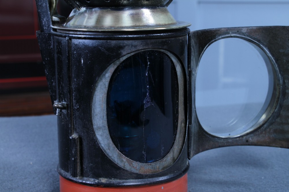An antique black painted iron GWR railway hand lantern featuring a circular glass lens, top handle, brass accents, and a red painted band near the base. View XII