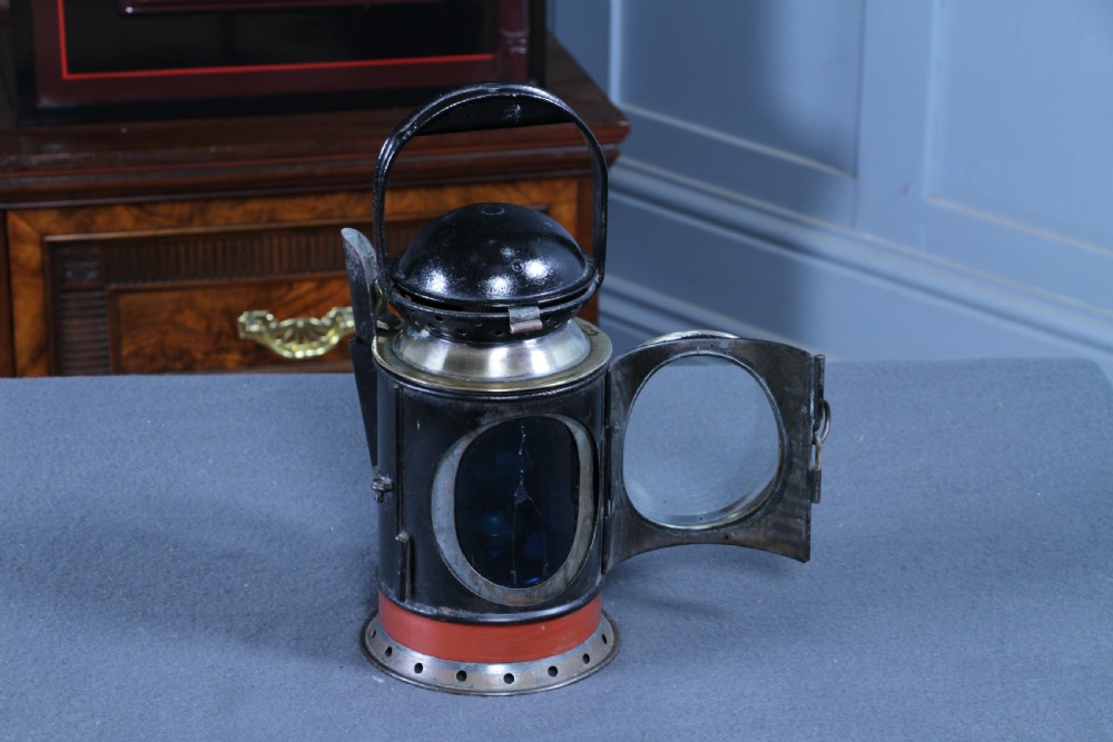 An antique black painted iron GWR railway hand lantern featuring a circular glass lens, top handle, brass accents, and a red painted band near the base. View XIII