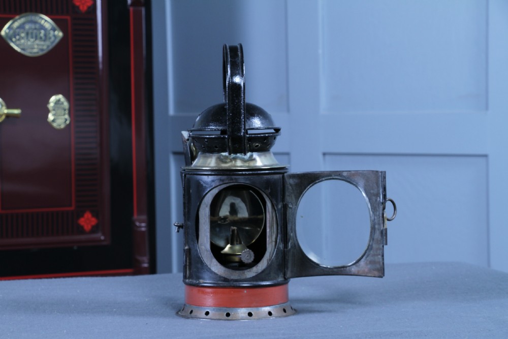 An antique black painted iron GWR railway hand lantern featuring a circular glass lens, top handle, brass accents, and a red painted band near the base. View XIV
