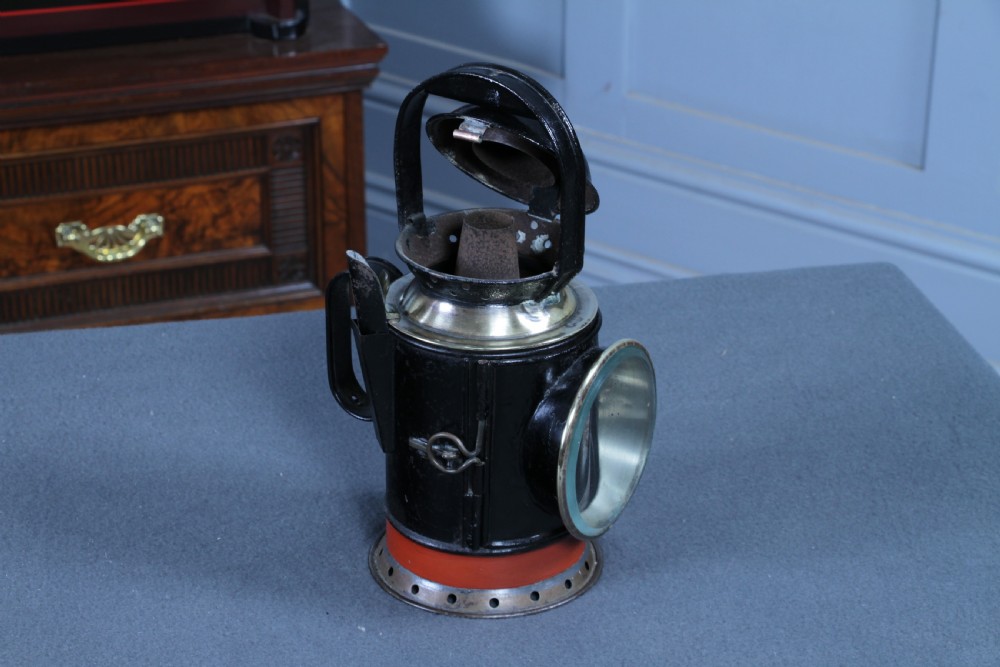 An antique black painted iron GWR railway hand lantern featuring a circular glass lens, top handle, brass accents, and a red painted band near the base. View XVI