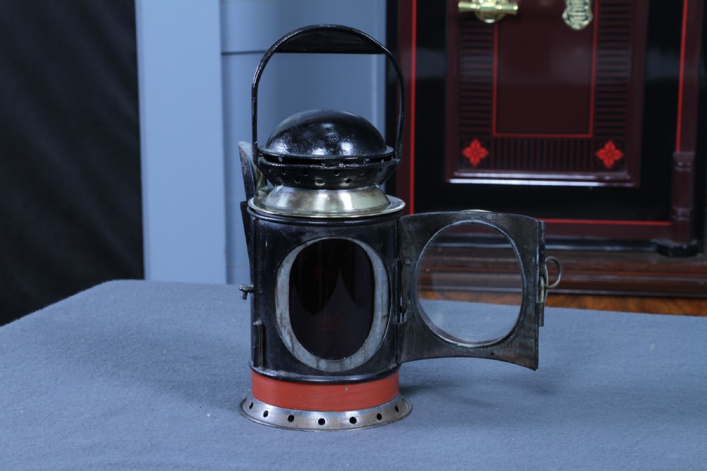 An antique black painted iron GWR railway hand lantern featuring a circular glass lens, top handle, brass accents, and a red painted band near the base. View XVII
