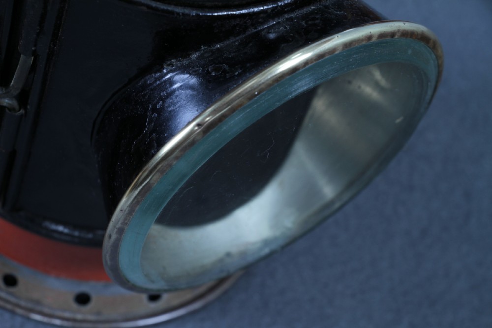 An antique black painted iron GWR railway hand lantern featuring a circular glass lens, top handle, brass accents, and a red painted band near the base. View XXIV