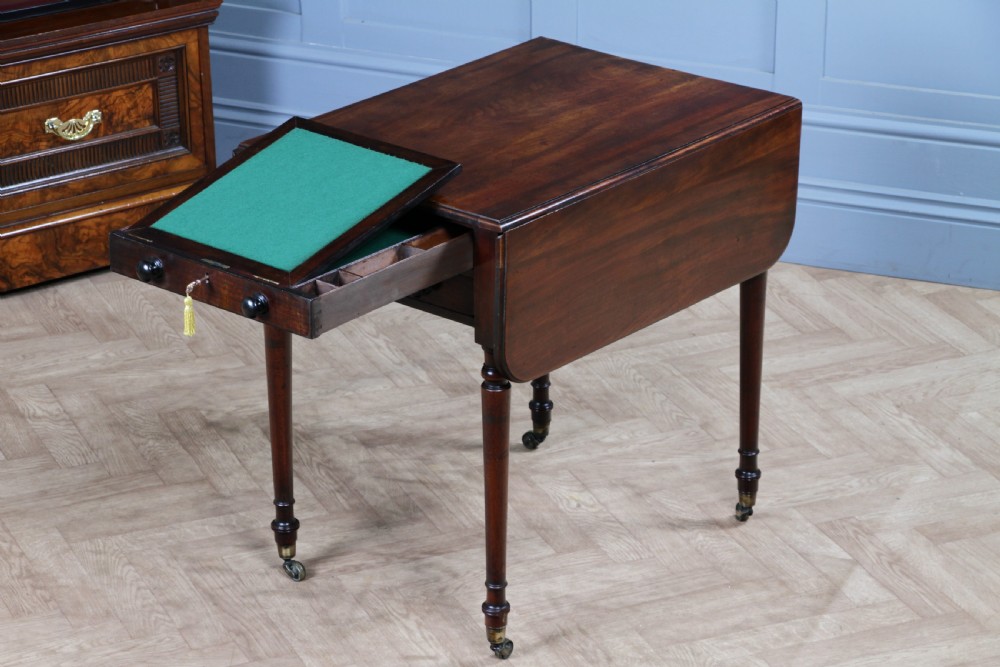 A George III mahogany Pembroke table featuring drop leaves, turned legs on brass castors, and an open drawer fitted with a green baize writing slope and compartments.