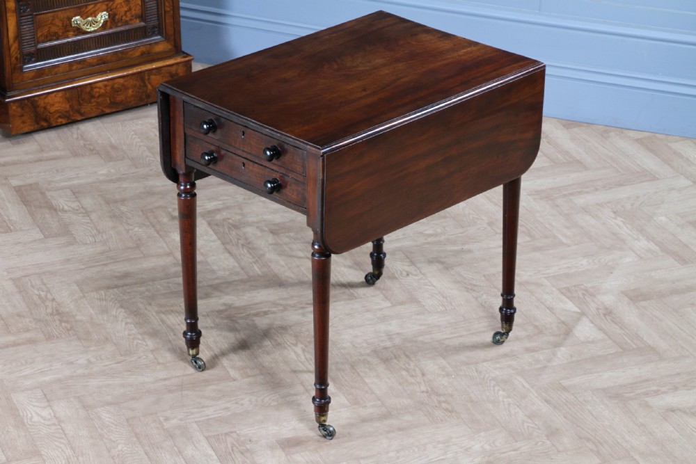 A George III mahogany Pembroke table featuring drop leaves, turned legs on brass castors, and an open drawer fitted with a green baize writing slope and compartments. View II