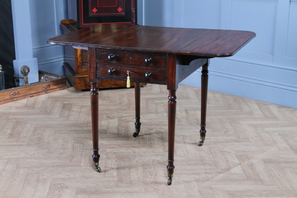 A George III mahogany Pembroke table featuring drop leaves, turned legs on brass castors, and an open drawer fitted with a green baize writing slope and compartments. View III
