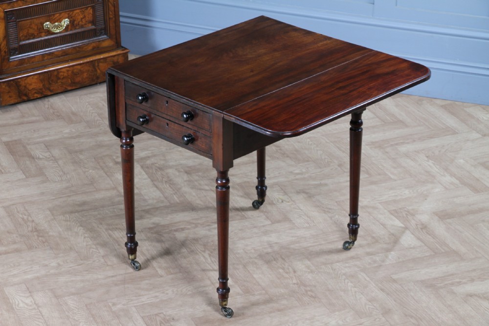 A George III mahogany Pembroke table featuring drop leaves, turned legs on brass castors, and an open drawer fitted with a green baize writing slope and compartments. View IV