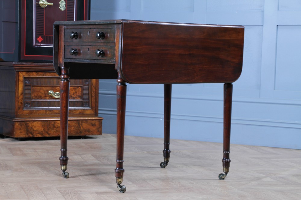 A George III mahogany Pembroke table featuring drop leaves, turned legs on brass castors, and an open drawer fitted with a green baize writing slope and compartments. View V