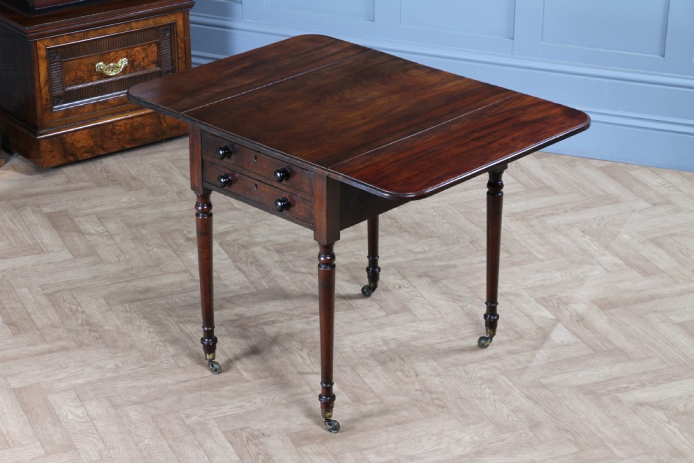 A George III mahogany Pembroke table featuring drop leaves, turned legs on brass castors, and an open drawer fitted with a green baize writing slope and compartments. View VI