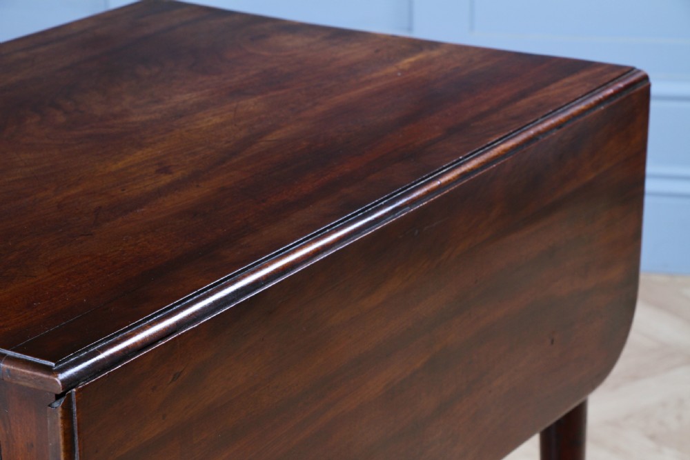 A George III mahogany Pembroke table featuring drop leaves, turned legs on brass castors, and an open drawer fitted with a green baize writing slope and compartments. View IX
