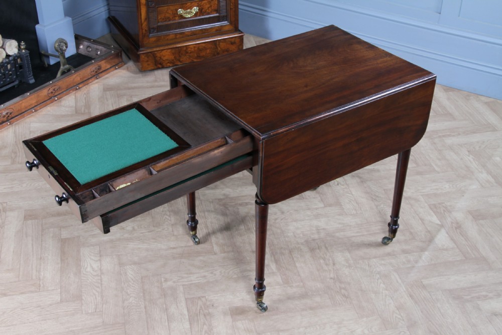 A George III mahogany Pembroke table featuring drop leaves, turned legs on brass castors, and an open drawer fitted with a green baize writing slope and compartments. View XXII