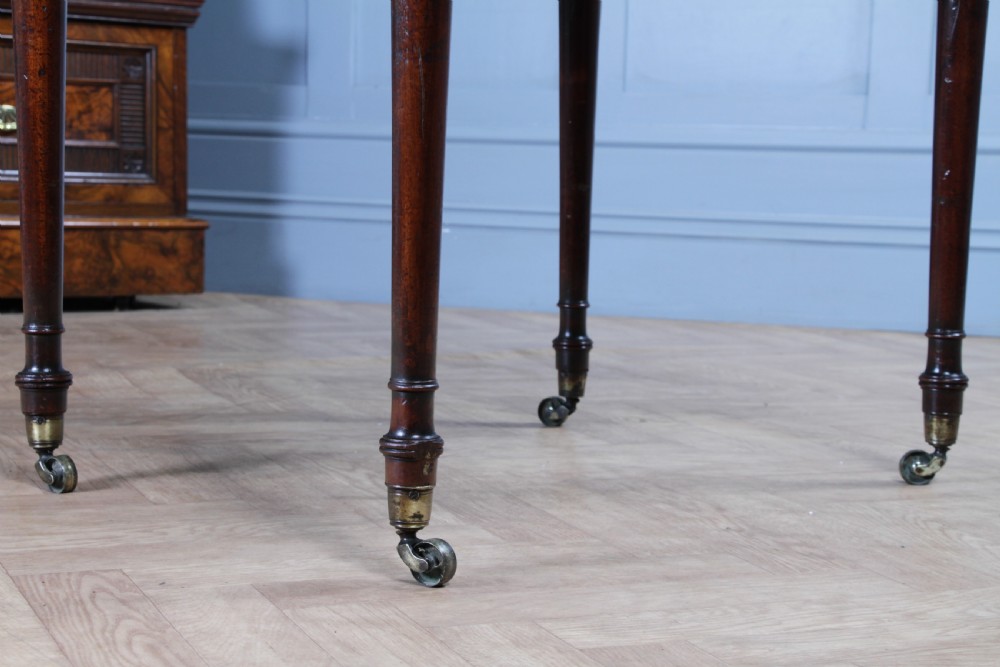 A George III mahogany Pembroke table featuring drop leaves, turned legs on brass castors, and an open drawer fitted with a green baize writing slope and compartments. View XXIV