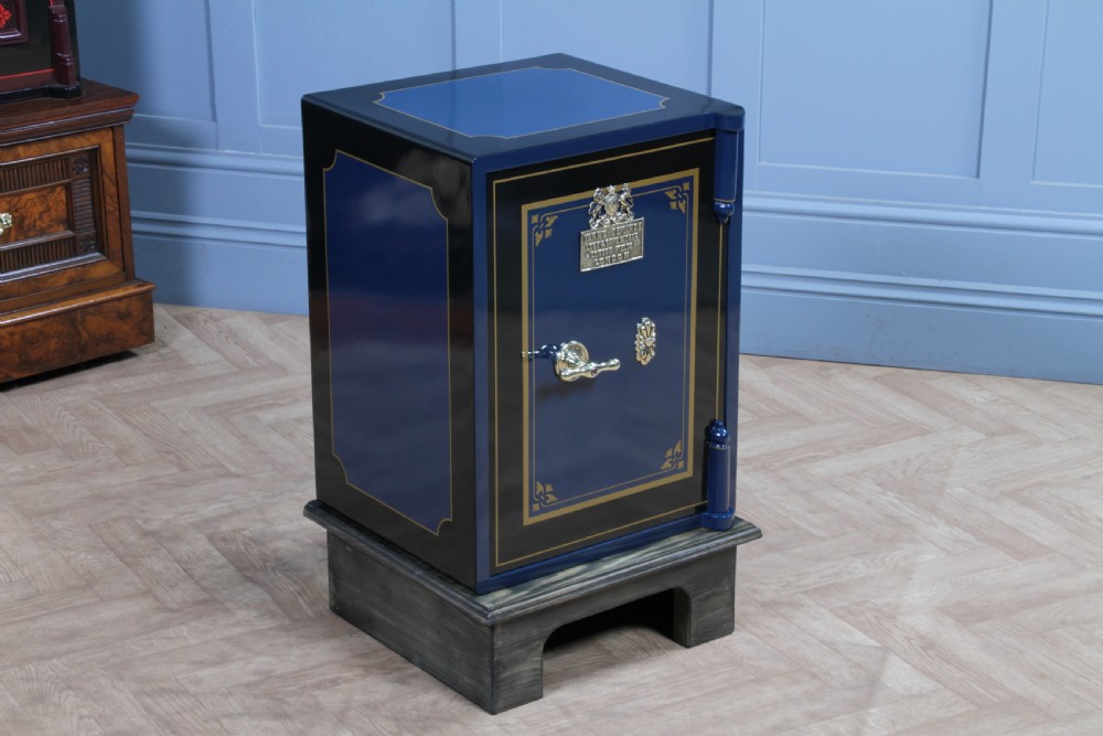 A restored Victorian navy blue and black cast iron safe featuring polished brass hardware and a makers plaque, raised on a dark wooden plinth. View II