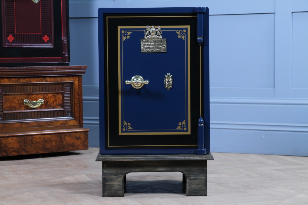 A restored Victorian navy blue and black cast iron safe featuring polished brass hardware and a makers plaque, raised on a dark wooden plinth. View III