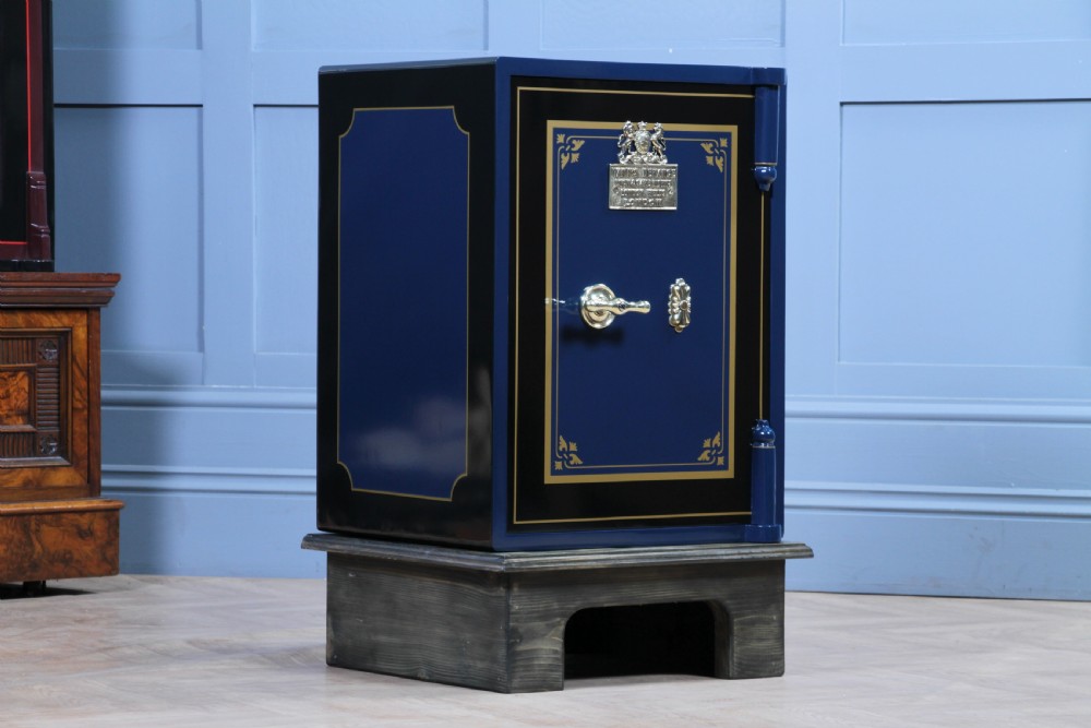 A restored Victorian navy blue and black cast iron safe featuring polished brass hardware and a makers plaque, raised on a dark wooden plinth. View IV