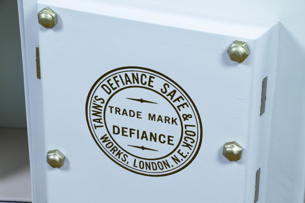 A restored Victorian navy blue and black cast iron safe featuring polished brass hardware and a makers plaque, raised on a dark wooden plinth. View IX