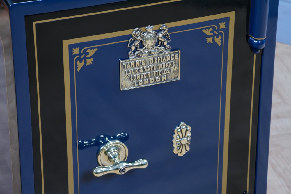 A restored Victorian navy blue and black cast iron safe featuring polished brass hardware and a makers plaque, raised on a dark wooden plinth. View XI