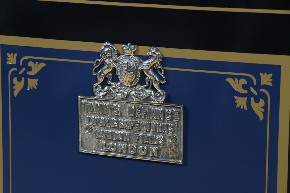A restored Victorian navy blue and black cast iron safe featuring polished brass hardware and a makers plaque, raised on a dark wooden plinth. View XII