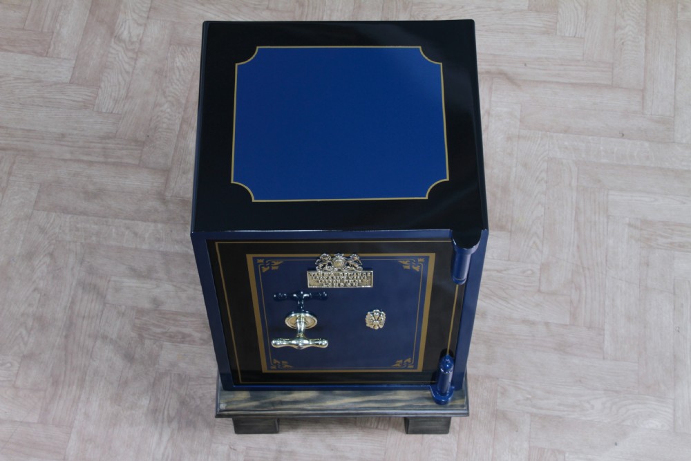 A restored Victorian navy blue and black cast iron safe featuring polished brass hardware and a makers plaque, raised on a dark wooden plinth. View XV