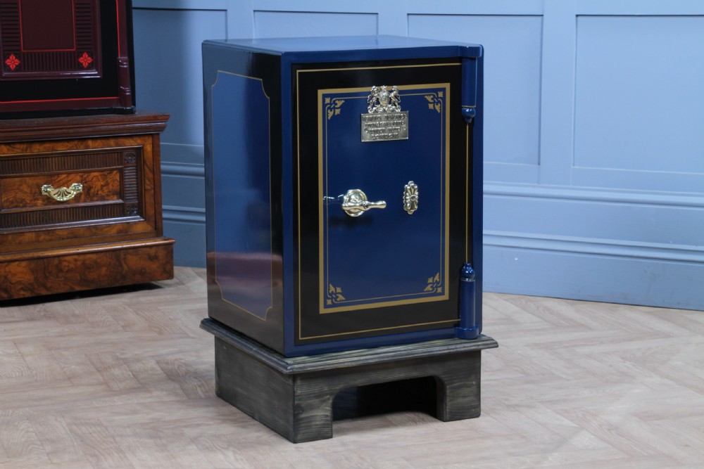A restored Victorian navy blue and black cast iron safe featuring polished brass hardware and a makers plaque, raised on a dark wooden plinth. View XVI