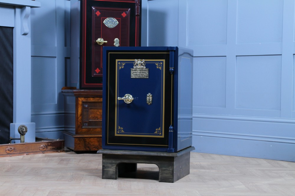 A restored Victorian navy blue and black cast iron safe featuring polished brass hardware and a makers plaque, raised on a dark wooden plinth. View XVII