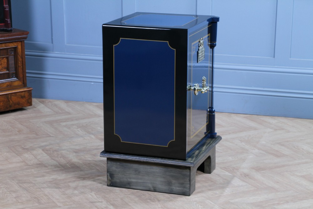 A restored Victorian navy blue and black cast iron safe featuring polished brass hardware and a makers plaque, raised on a dark wooden plinth. View XVIII