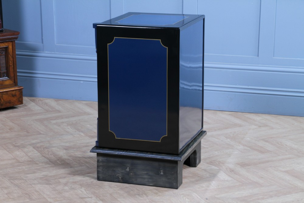 A restored Victorian navy blue and black cast iron safe featuring polished brass hardware and a makers plaque, raised on a dark wooden plinth. View XIX